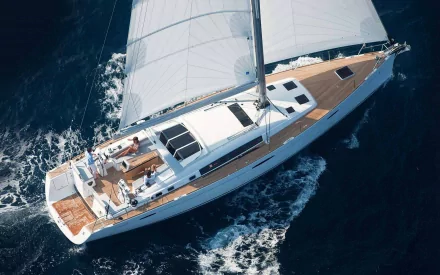 HD desktop wallpaper of a sleek yacht sailing on deep blue water, showcasing white sails and wooden deck details from an aerial perspective.