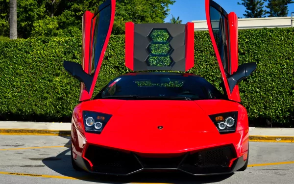 HD desktop wallpaper featuring a red Lamborghini Murcielago with its scissor doors open, set against a backdrop of greenery and clear blue sky.