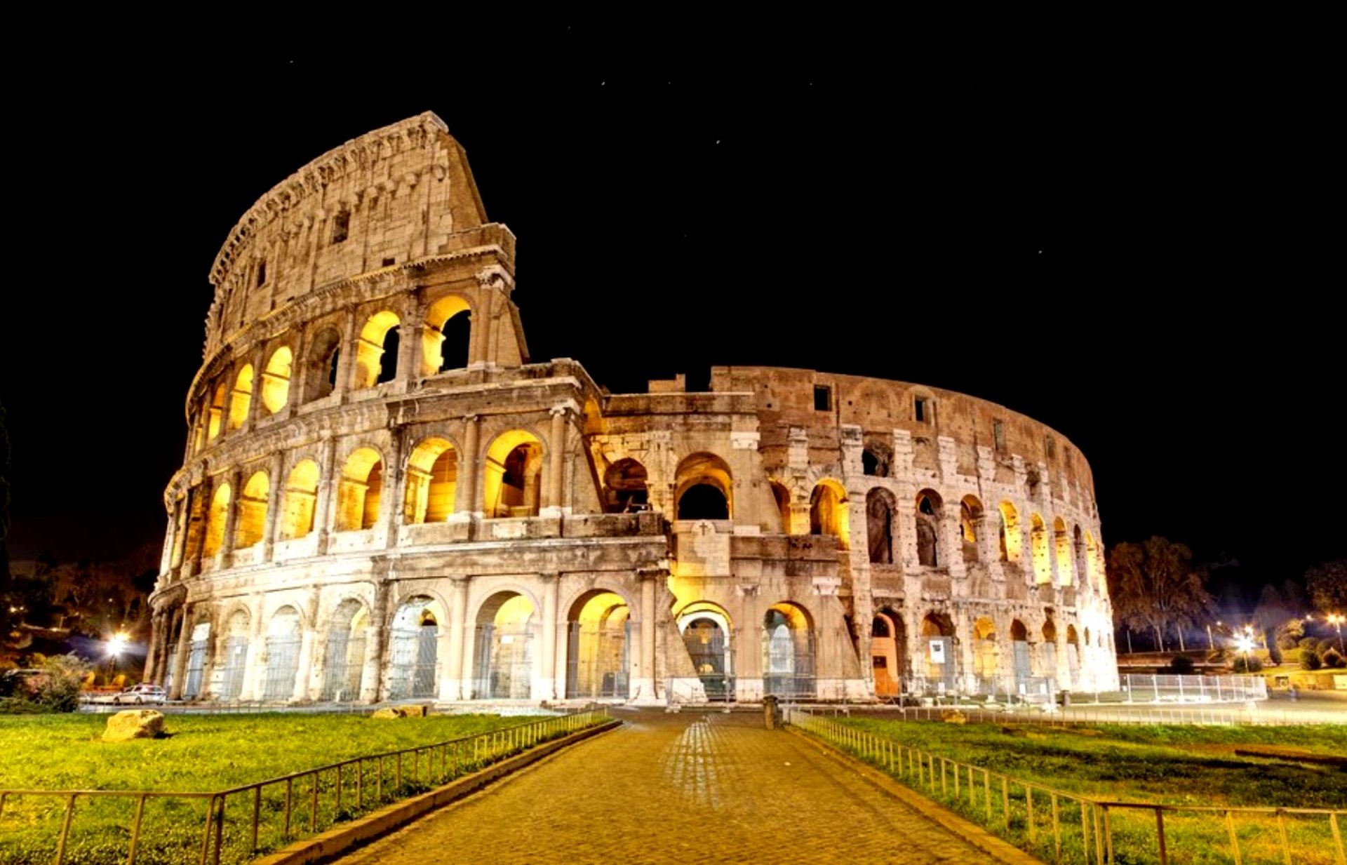 HD PC desktop wallpaper of the illuminated man-made Roman Colosseum at night, wide-angle view of the ancient amphitheater against a dark sky.