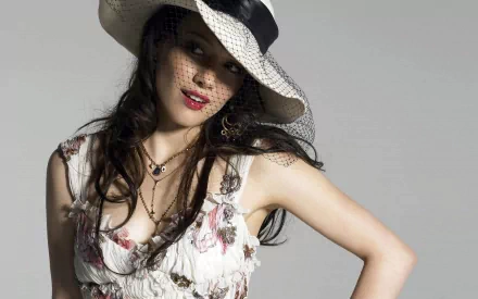 HD desktop wallpaper featuring celebrity Hilary Duff wearing a floral dress and wide-brimmed hat with a netted veil against a neutral background.