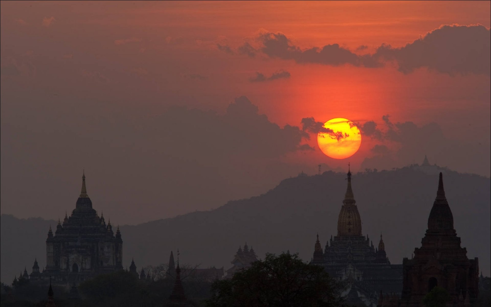HD PC desktop wallpaper showing a serene religious temple silhouette against a vibrant orange sunset sky with distant hills.