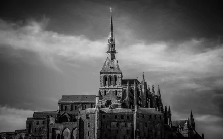 Religious Mont Saint-Michel abbey rising beneath dramatic clouds — black-and-white HD PC desktop wallpaper and background showcasing the island monastery's spire and Gothic architecture.