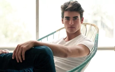 HD desktop wallpaper featuring a man with striking features, relaxing in a modern chair. The serene backdrop and natural light accentuate his handsome appearance, making for a beautifully composed scene.