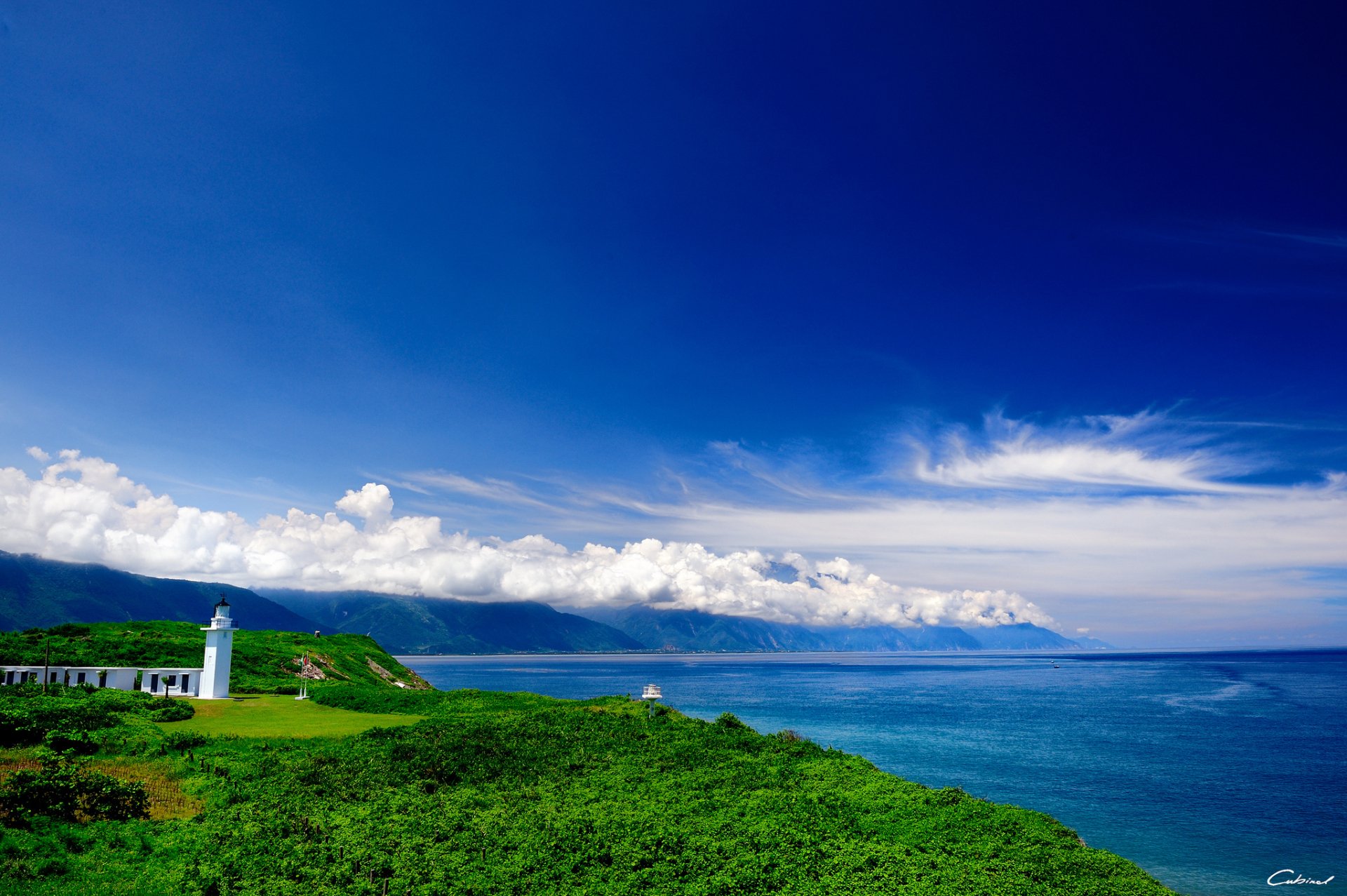 HD photography of a lush green coastline with a white lighthouse under a vibrant blue sky, captured as a stunning PC desktop wallpaper and background.