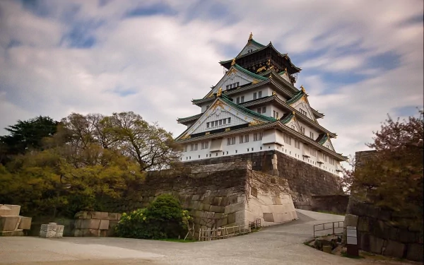 HD desktop wallpaper showcasing the historic man-made Osaka Castle surrounded by trees under a cloudy sky.