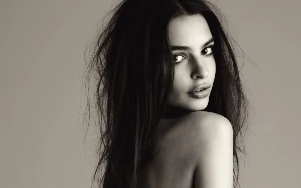 Black and white HD wallpaper featuring Emily Ratajkowski, capturing her in a striking pose with tousled hair and a captivating expression.