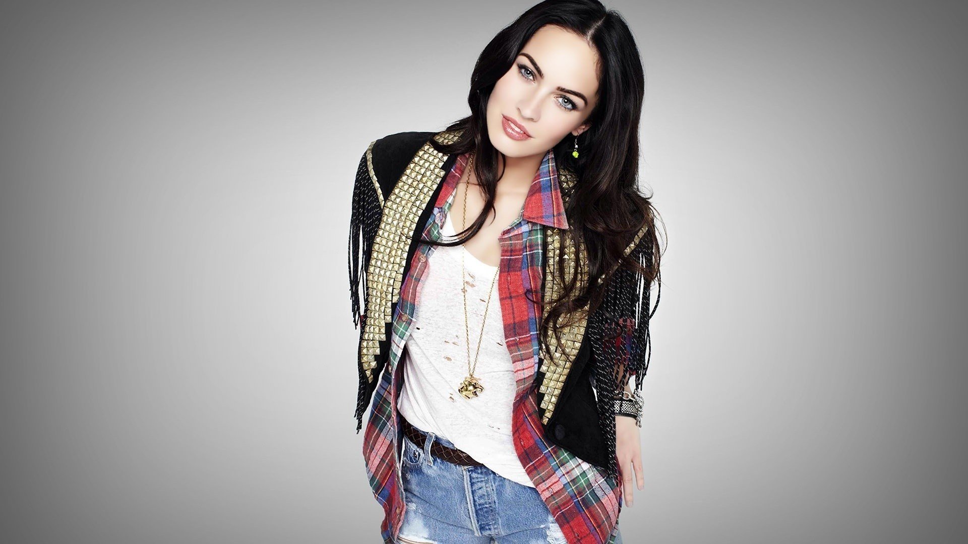 Megan Fox poses confidently in a stylish outfit with a layered look, featuring a plaid shirt and denim. This HD desktop wallpaper showcases her striking features against a neutral background.