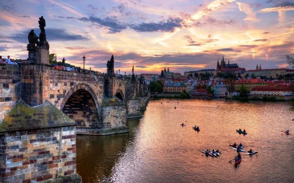 A stunning HD wallpaper of Prague at sunset, featuring the iconic Charles Bridge and boats on the river, capturing the city's beautiful architecture and serene atmosphere.