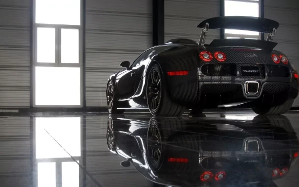 HD desktop wallpaper featuring a Bugatti Veyron parked indoors. The sleek, black vehicle reflects on the polished floor, highlighted by soft natural light from large windows in the background.