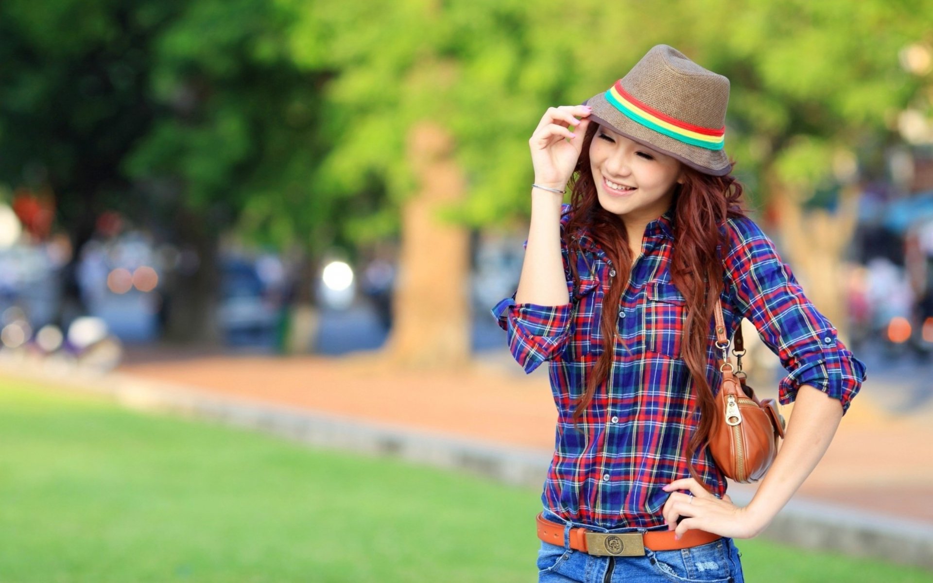 HD wallpaper of an Asian woman in a plaid shirt and hat, smiling and posing confidently outdoors with a blurred green background.