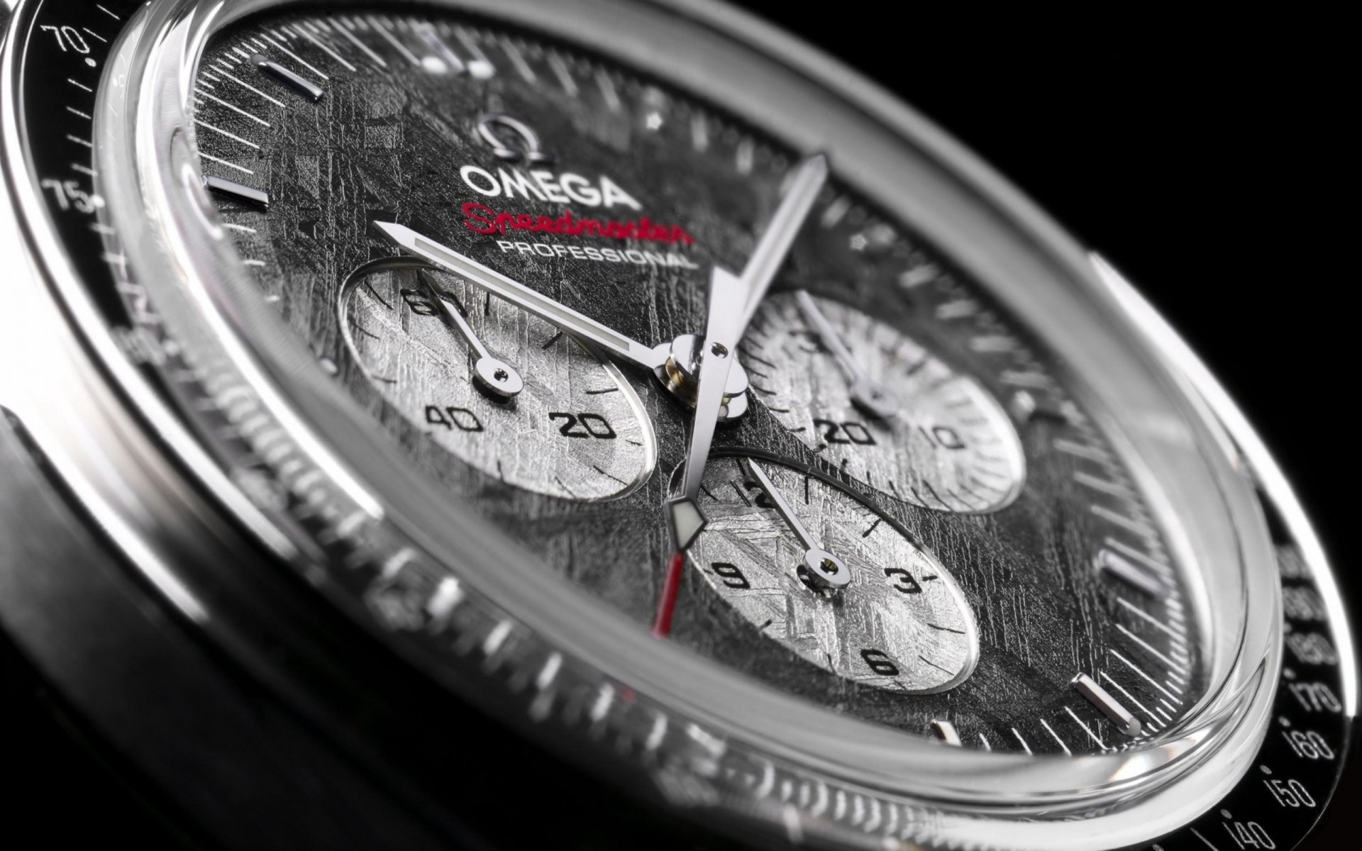 Close-up of a man-made Omega chronograph watch face with textured dial and stainless-steel case, red-tipped hand — 2K Quad HD PC desktop wallpaper/background.