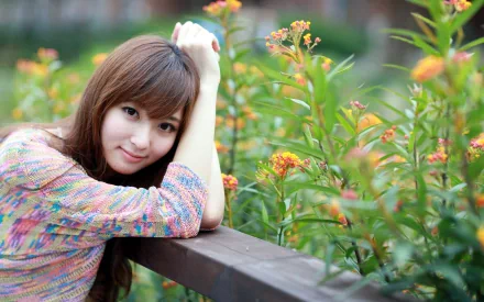 An Asian woman leaning on a wooden railing, surrounded by vibrant green plants and orange flowers, creating a serene and colorful HD desktop wallpaper and background.