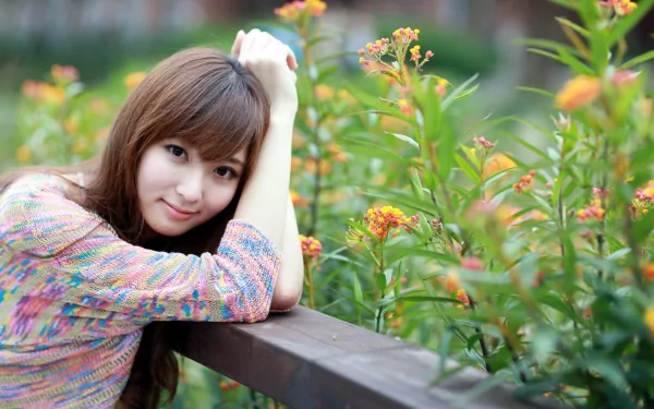 An Asian woman leaning on a wooden railing, surrounded by vibrant green plants and orange flowers, creating a serene and colorful HD desktop wallpaper and background.