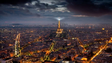 HD PC desktop wallpaper: aerial night view of Paris, man-made cityscape with illuminated Eiffel Tower and glowing streets under dramatic clouds.