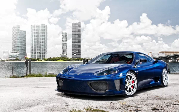 A blue Ferrari 360 Modena supercar parked by the waterfront with modern city skyscrapers in the background, showcased in 4K Ultra HD quality.