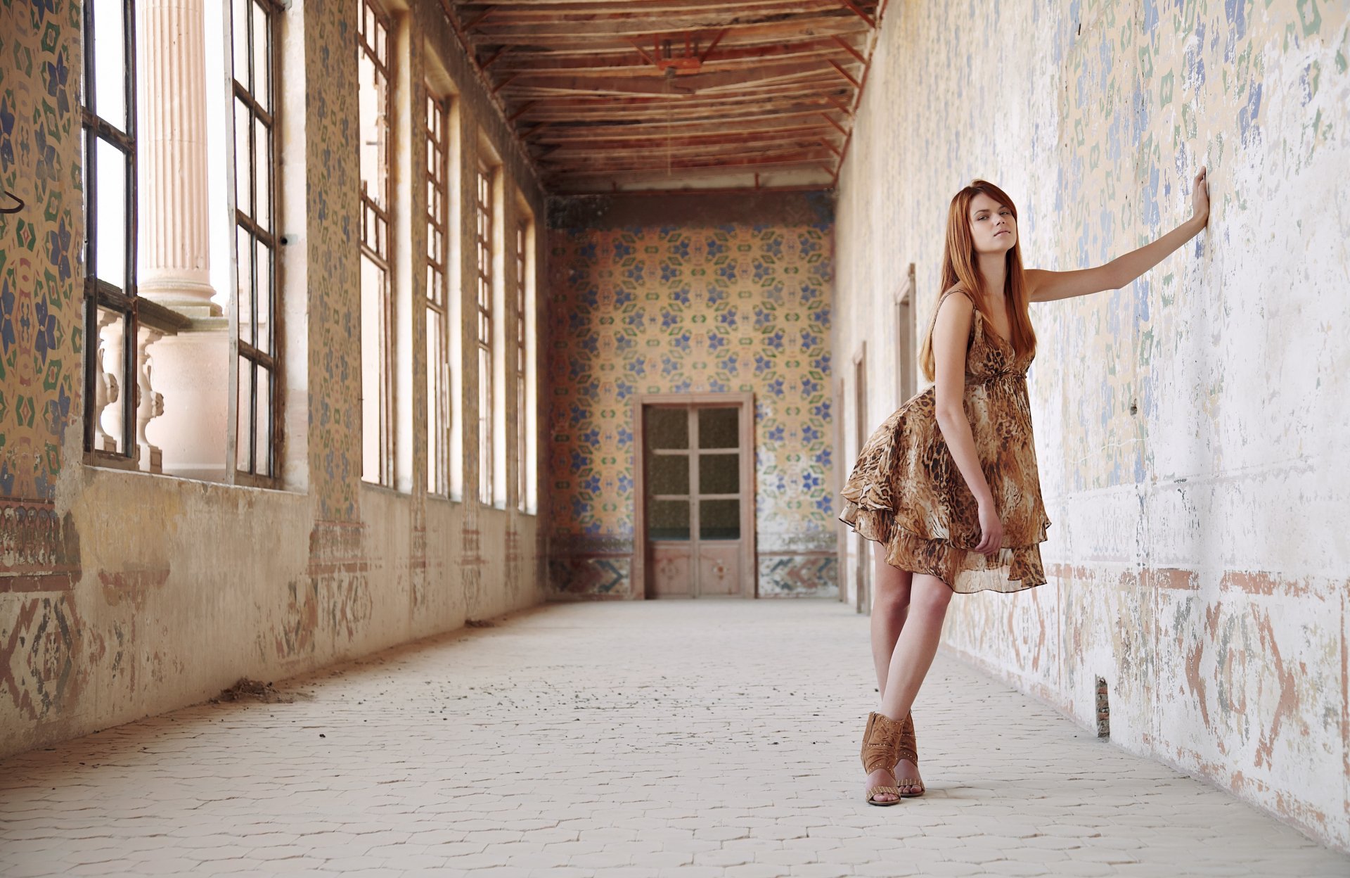 A woman model in a patterned dress poses in a sunlit, ornate hallway with weathered walls, providing a stunning HD desktop wallpaper and background.