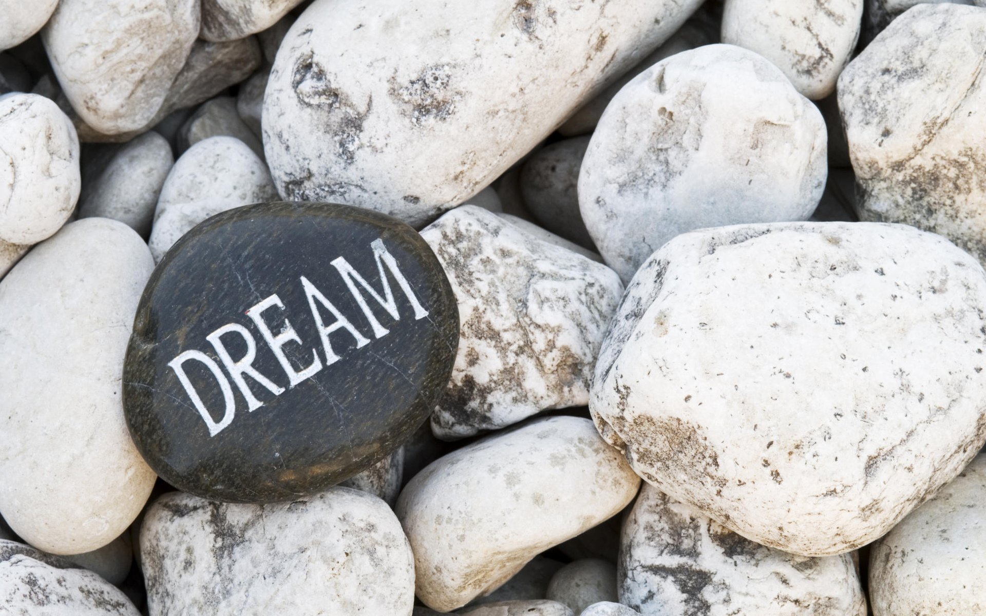 HD nature desktop wallpaper featuring a collection of smooth white rocks with one black rock engraved with the word DREAM in white letters.