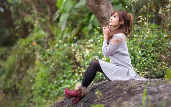 A woman with Asian features sits thoughtfully on a rock in a lush, green forest, wearing a grey dress, black leggings, and red boots. HD desktop wallpaper and background.