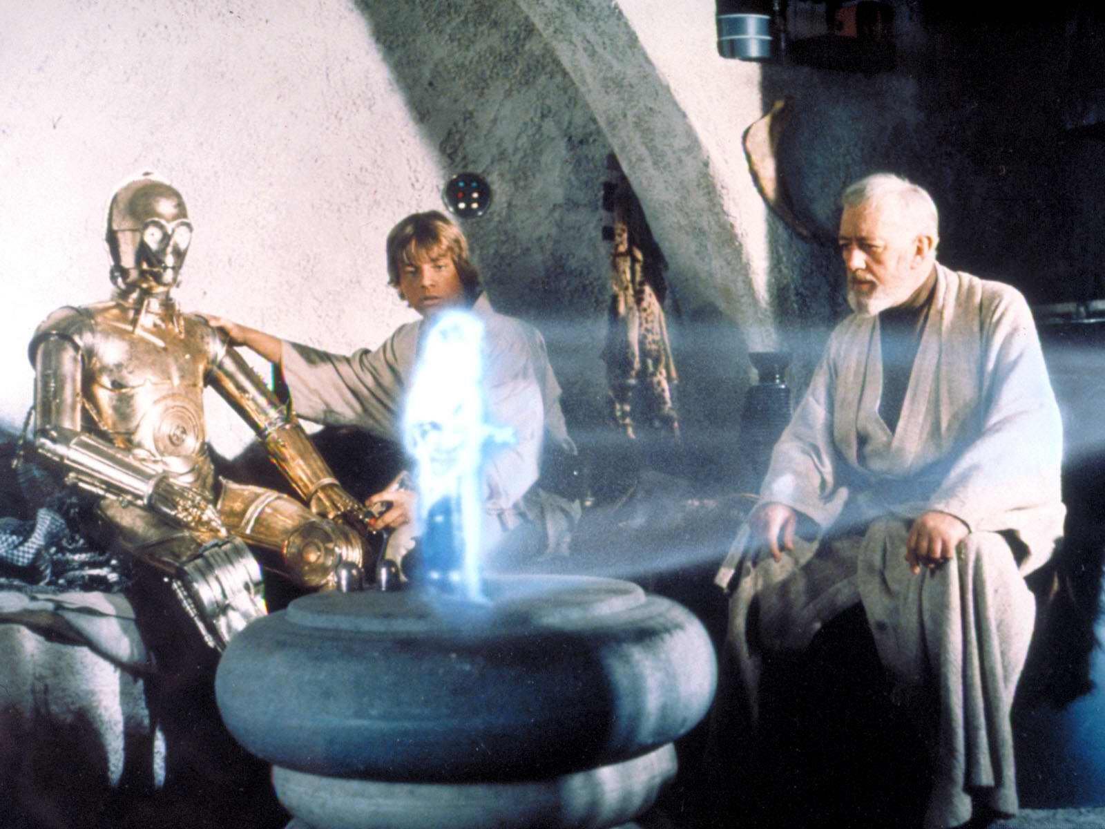 HD PC desktop wallpaper/background: Star Wars movie scene — a golden protocol droid, a young Jedi and an elderly mentor gathered around a glowing blue hologram in a sandstone chamber.