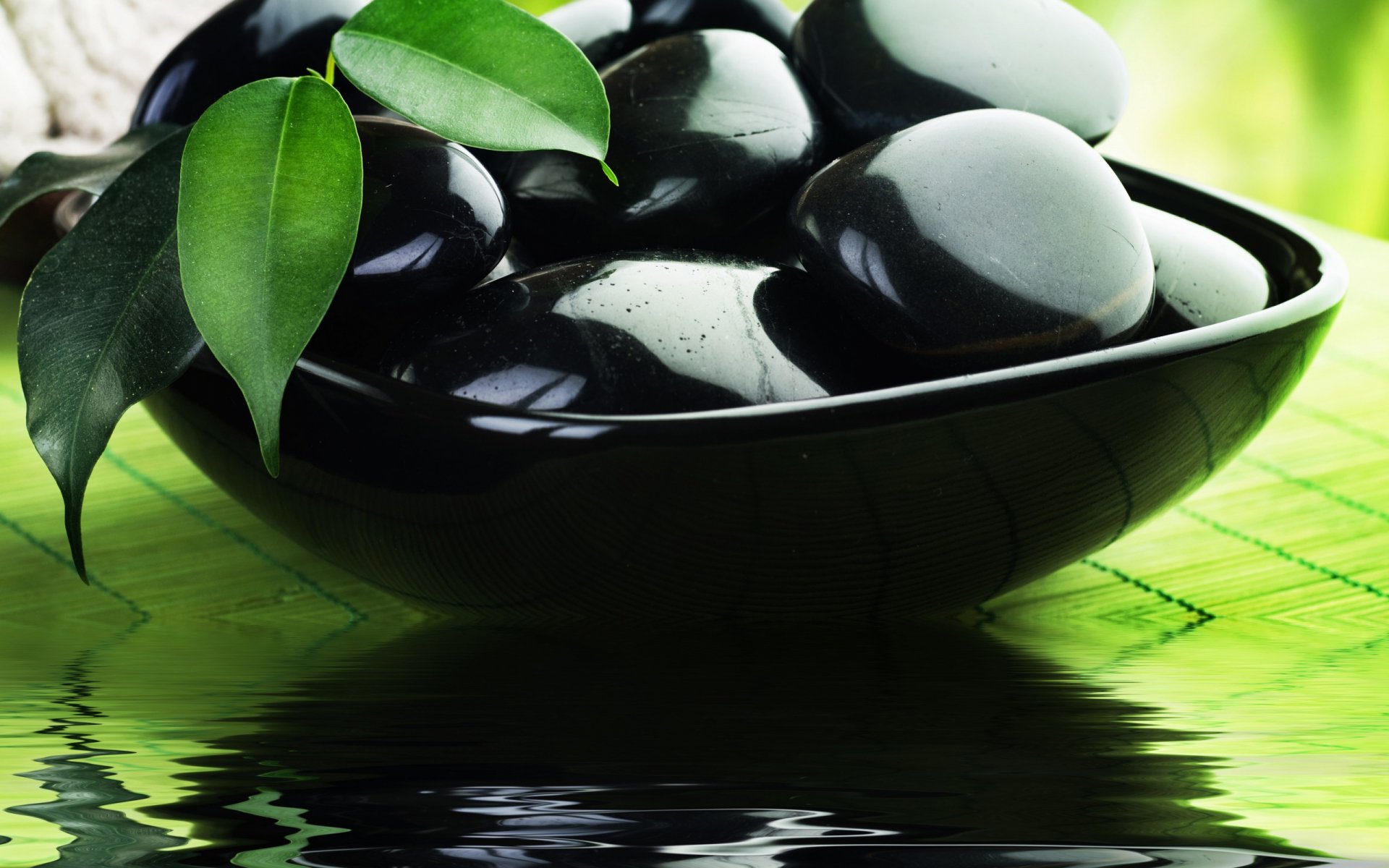 HD desktop wallpaper featuring smooth black stones resting in a dark bowl with green leaves, set against a bright, natural background reflecting calm and nature.