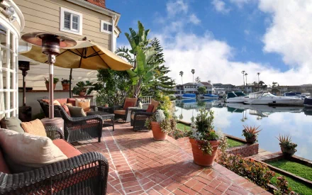 HD desktop wallpaper of a man-made terrace with wicker furniture, potted plants, and umbrellas overlooking a calm marina under a partly cloudy sky.