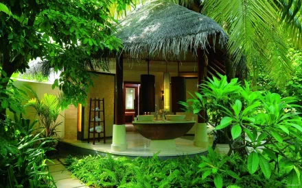 A serene spa hut nestled among lush greenery, featuring an inviting bath area and surrounded by tropical plants. This HD wallpaper captures a tranquil atmosphere.