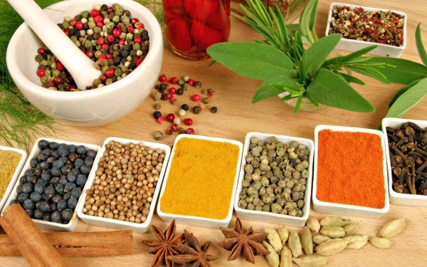 A vibrant display of various herbs and spices arranged in bowls and scattered across a wooden surface, showcasing the rich textures and colors of culinary ingredients in a high-definition background.