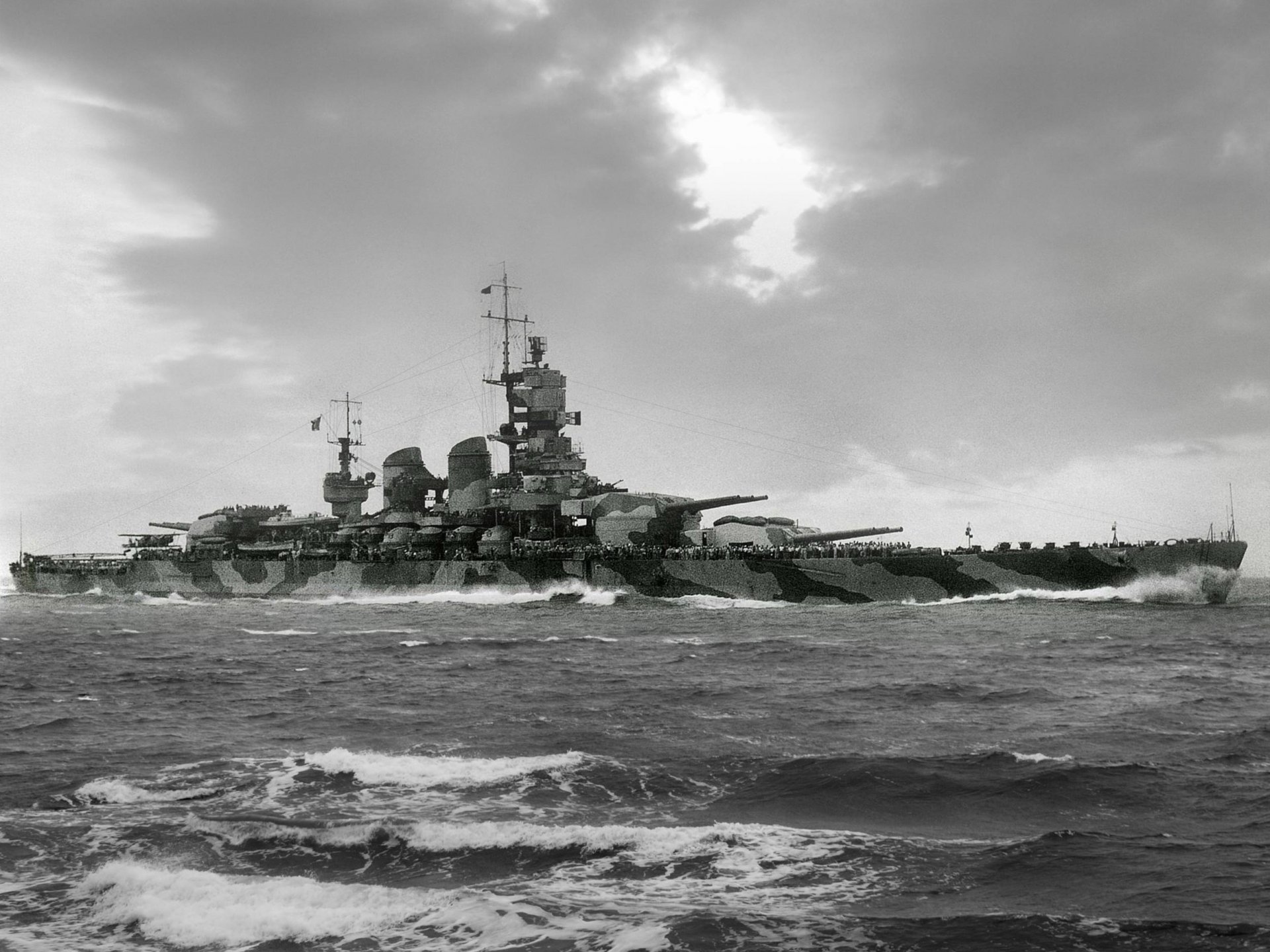 Black and white HD desktop wallpaper featuring a large military battleship sailing through choppy waters under a cloudy sky.
