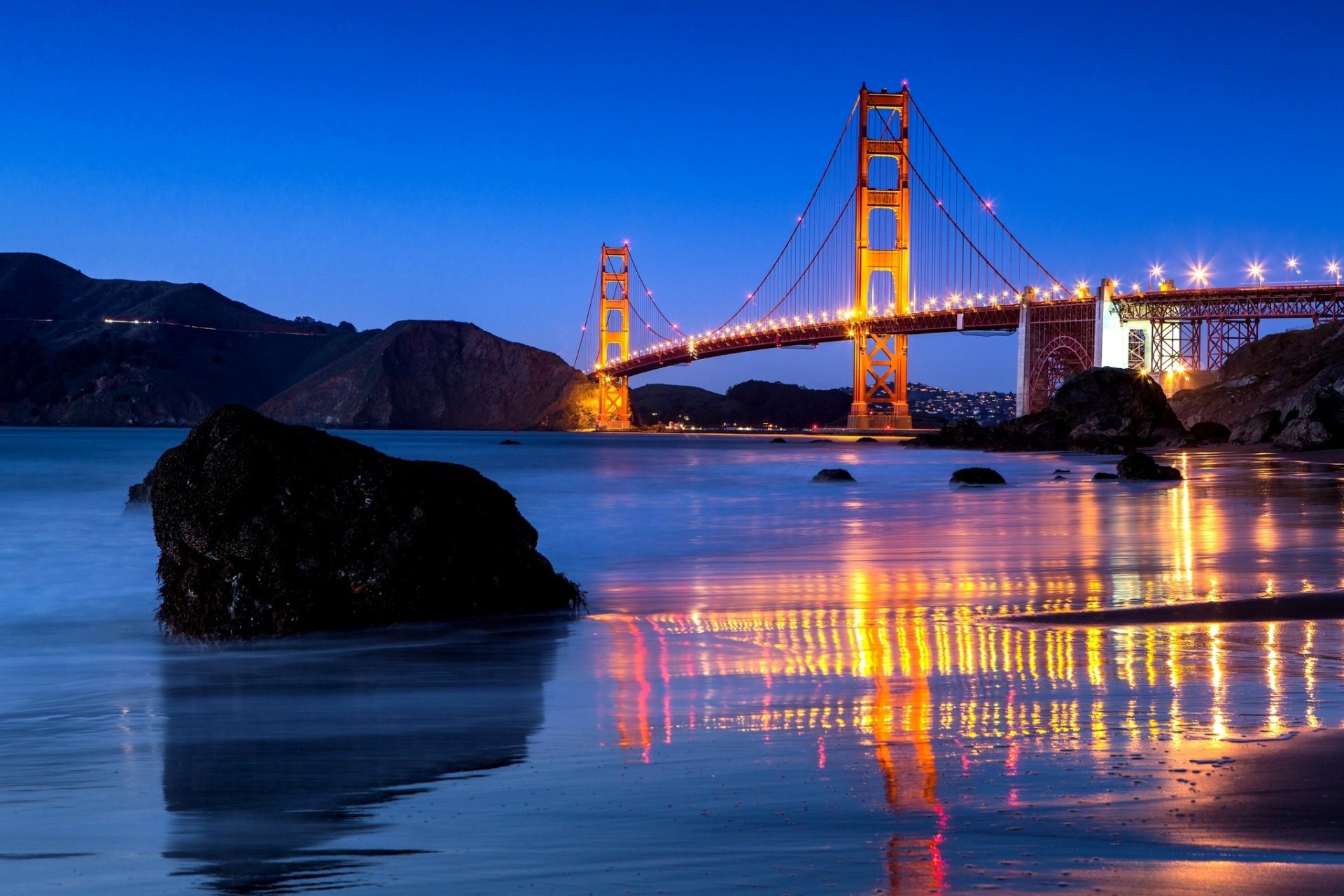 Man-made Golden Gate Bridge at dusk, illuminated towers and cables reflecting on calm bay waters — HD PC desktop wallpaper background.