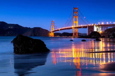 Man-made Golden Gate Bridge at dusk, illuminated towers and cables reflecting on calm bay waters — HD PC desktop wallpaper background.