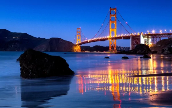 Man-made Golden Gate Bridge at dusk, illuminated towers and cables reflecting on calm bay waters — HD PC desktop wallpaper background.