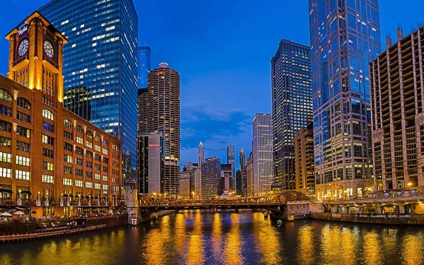 Chicago skyline at dusk with illuminated skyscrapers and a glowing bridge reflected in the river, showcasing a vibrant man-made urban scene.