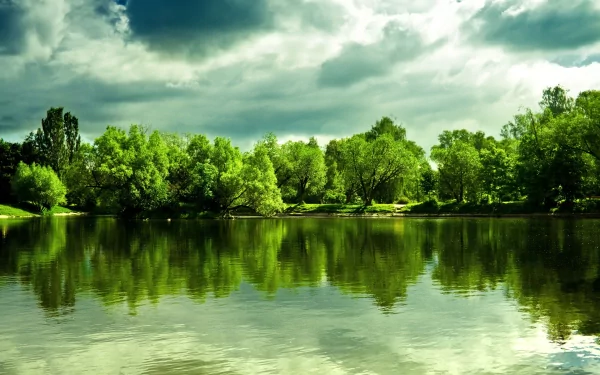Lush greenery and dramatic clouds reflect beautifully on a serene lake in this vibrant nature scene, showcasing stunning 4K Ultra HD detail for a captivating desktop wallpaper.