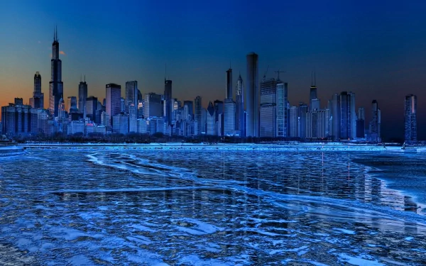 2K Quad HD PC desktop wallpaper: Chicago's man-made skyline at dusk, glowing skyscrapers reflected on an icy river beneath a deep blue sky.