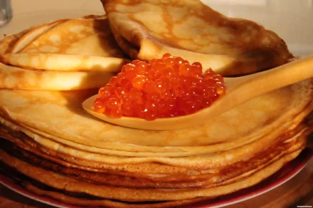 2K Quad HD PC desktop wallpaper: stack of golden crêpes on a plate with a spoonful of bright orange salmon caviar on top, close-up food background.