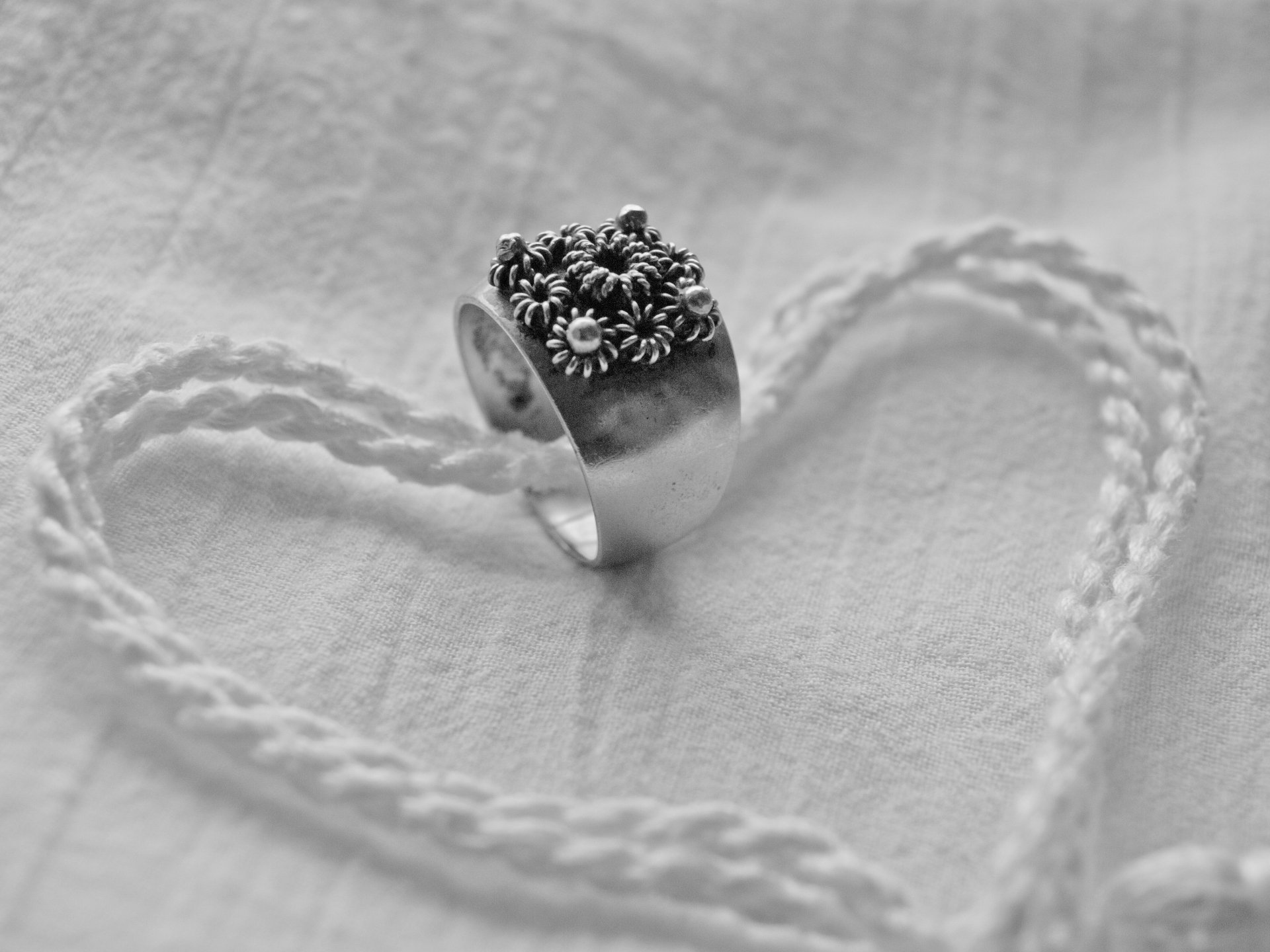 Artistic 4K Ultra HD wallpaper featuring a detailed ring placed inside a heart shape crafted from braided material on a textured background.