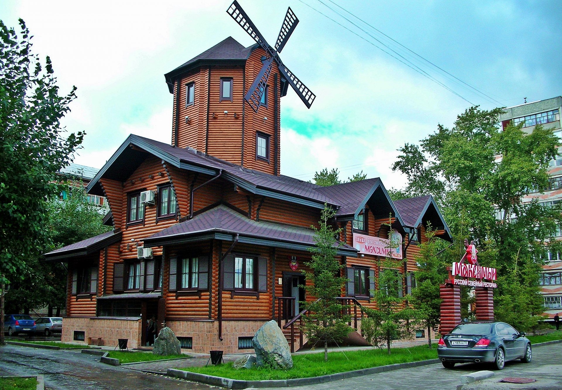 A striking wooden building featuring a windmill, surrounded by greenery and a parked car, serving as an engaging HD desktop wallpaper and background.