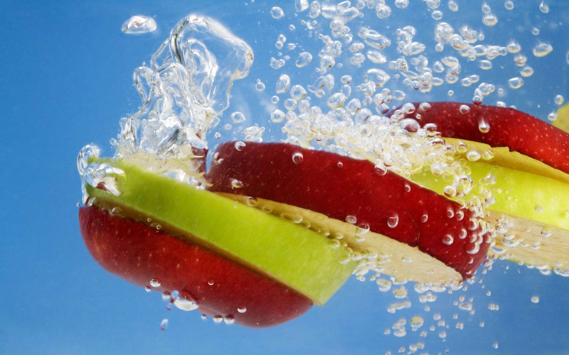 HD PC desktop wallpaper showing food: red and green apple slices splashing underwater with bubbles against a bright blue background.