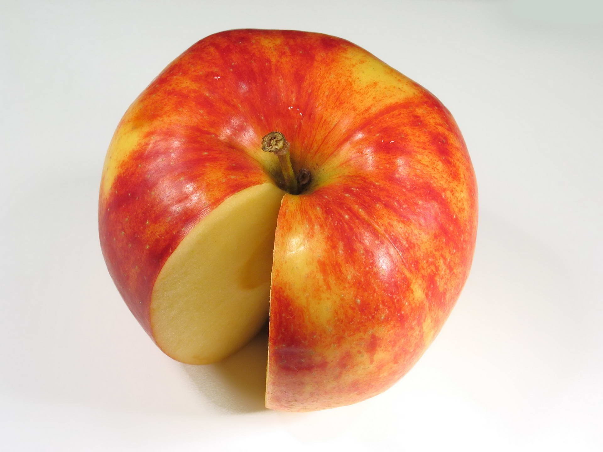 HD PC desktop wallpaper and background: glossy red-yellow apple with a wedge removed, pale flesh exposed on a clean white surface — food apple close-up.