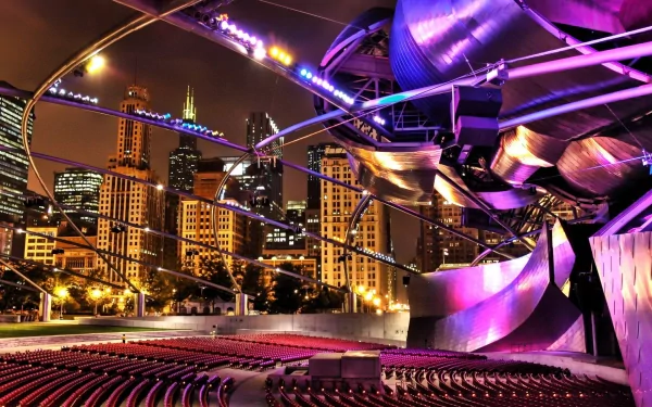 HD desktop wallpaper of Chicago's illuminated outdoor theater with sweeping metallic stage, empty seats and a glowing city skyline at night — man-made lights and architecture.