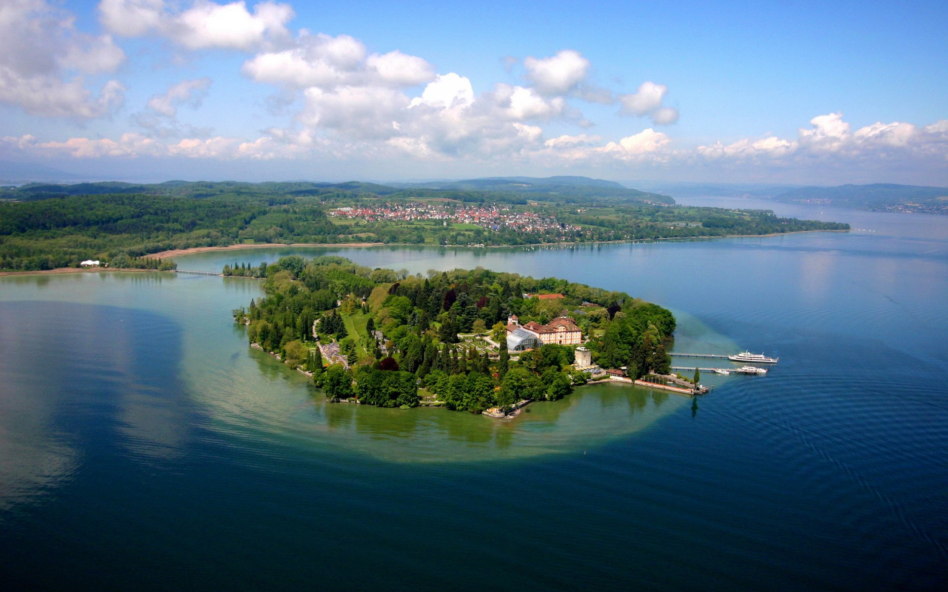 A stunning aerial view of a lush green island surrounded by tranquil blue waters, with hills and a quaint village in the background. A beautiful landscape for HD desktop wallpaper.