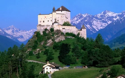 HD desktop wallpaper featuring the man-made Tarasp Castle perched on a hill with snowy mountains in the background under a clear blue sky.