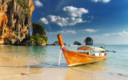 HD PC desktop wallpaper featuring a traditional wooden boat anchored on a clear, sandy beach with rocky cliffs and a bright blue sky in the background.