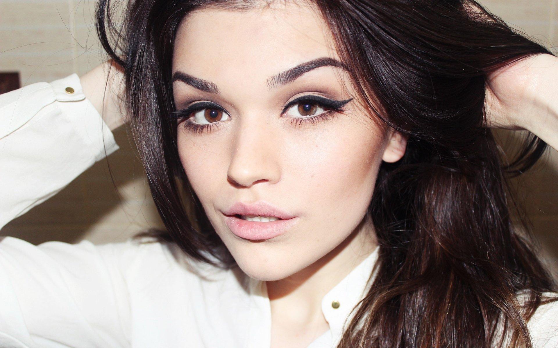 HD desktop wallpaper featuring a close-up of a beautiful woman with dark hair and expressive eyes, wearing a white top against a neutral background.