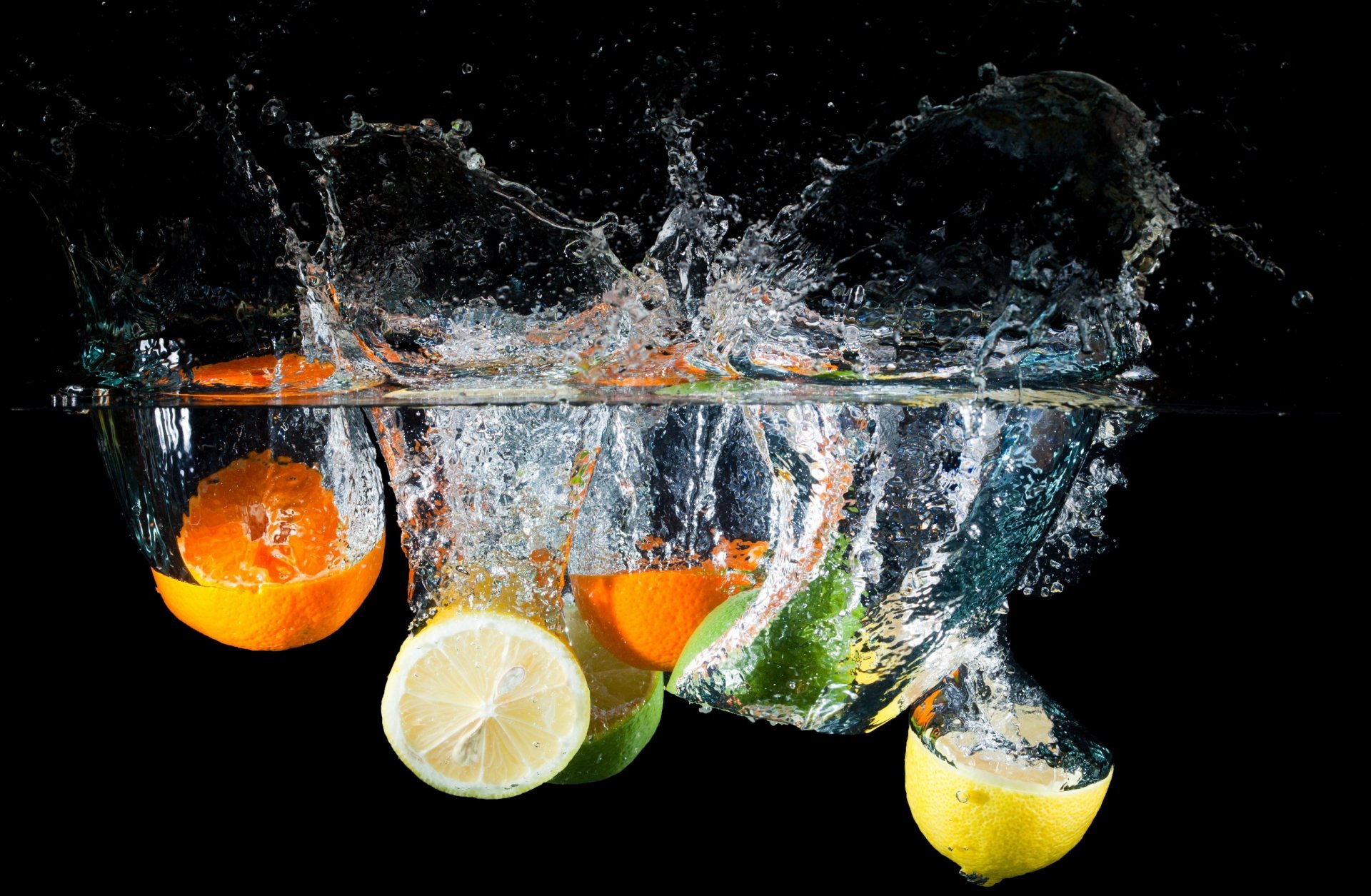 HD PC desktop wallpaper featuring vibrant citrus fruits—orange, lime, and lemon—splashing into clear water against a black background.