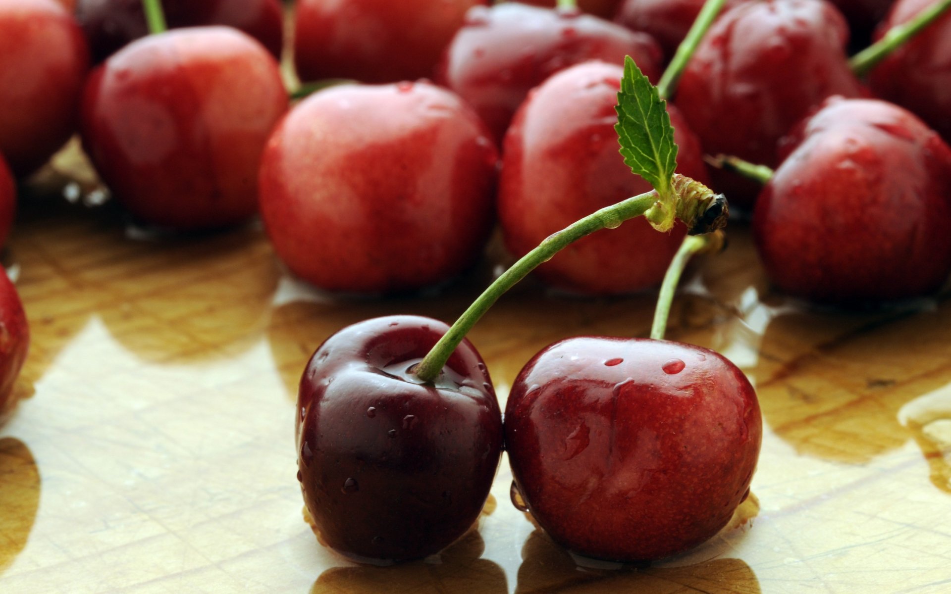 HD food desktop wallpaper featuring close-up of fresh, water-dropped cherries with green stems on a light surface.