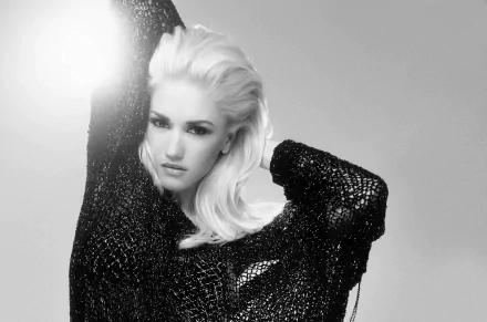Black and white HD desktop wallpaper featuring Gwen Stefani posing with her arm raised, showcasing her platinum blonde hair and textured black outfit.