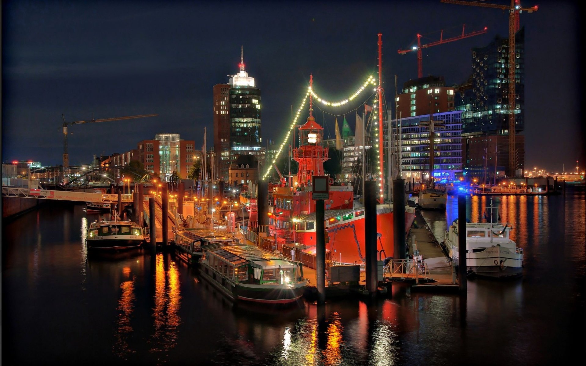 Nighttime view of Hamburg's harbor with illuminated ships and city skyline, showcasing man-made structures reflected in calm water, captured in HD for desktop wallpaper.
