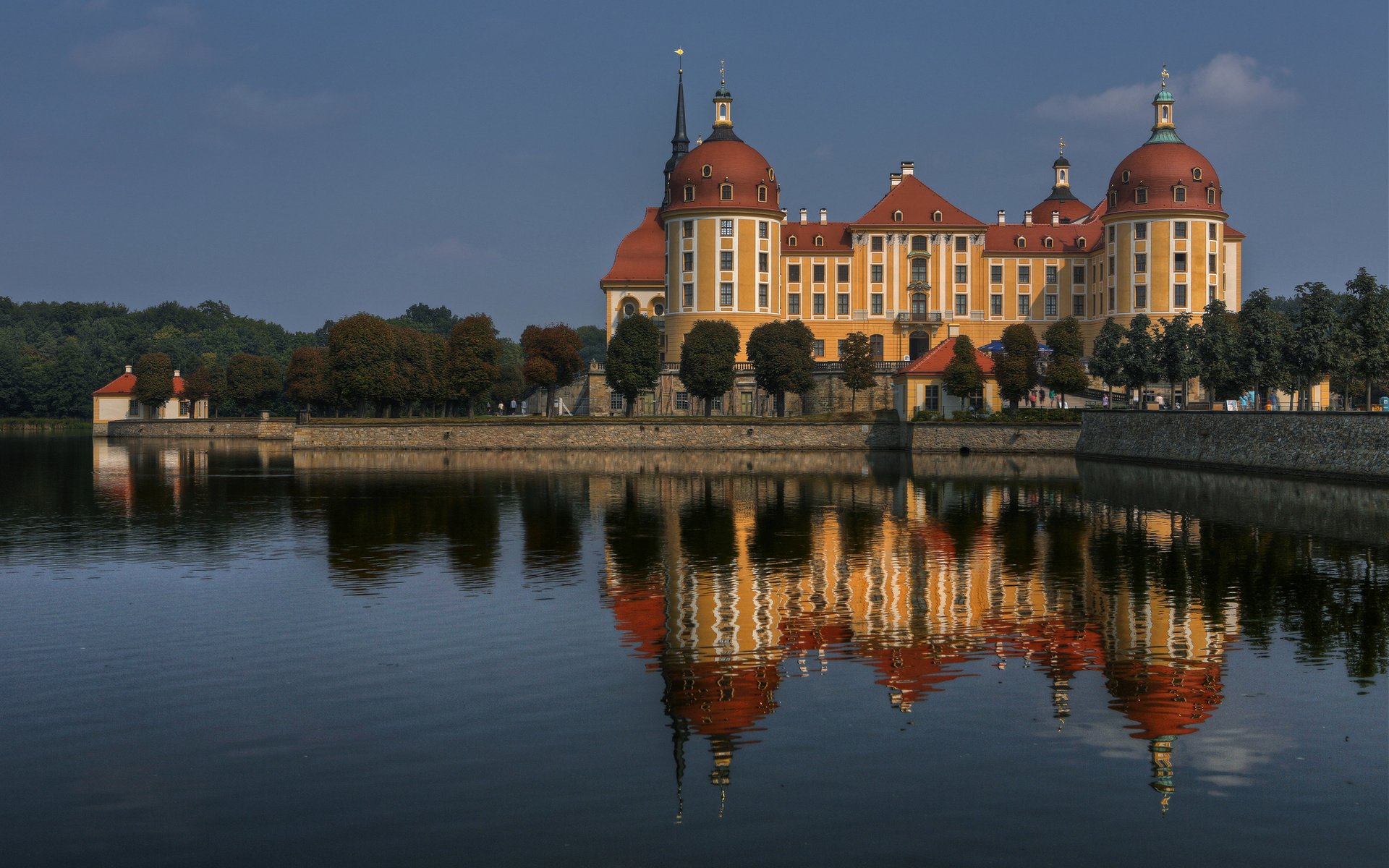 HD desktop wallpaper showing a grand man-made castle with domed towers reflected in calm water under a clear sky.