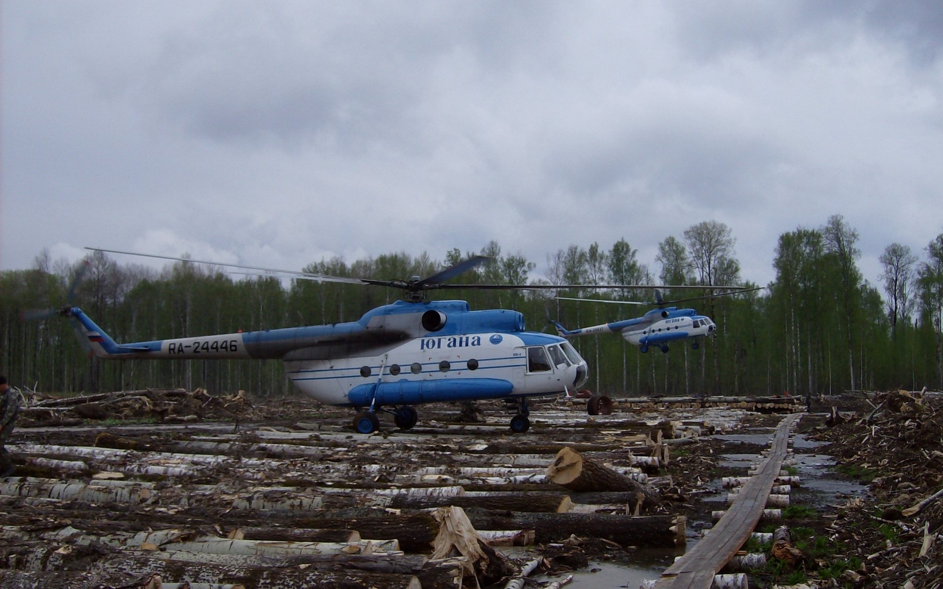 HD PC desktop wallpaper showing a Mil Mi-8 helicopter on a cleared forest area under a cloudy sky.